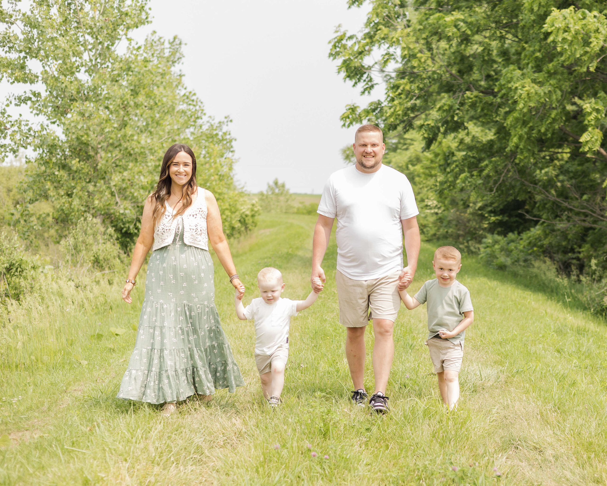 Happy toddler brothers walk a park trail holding hands with mom and dad in green and white outfits