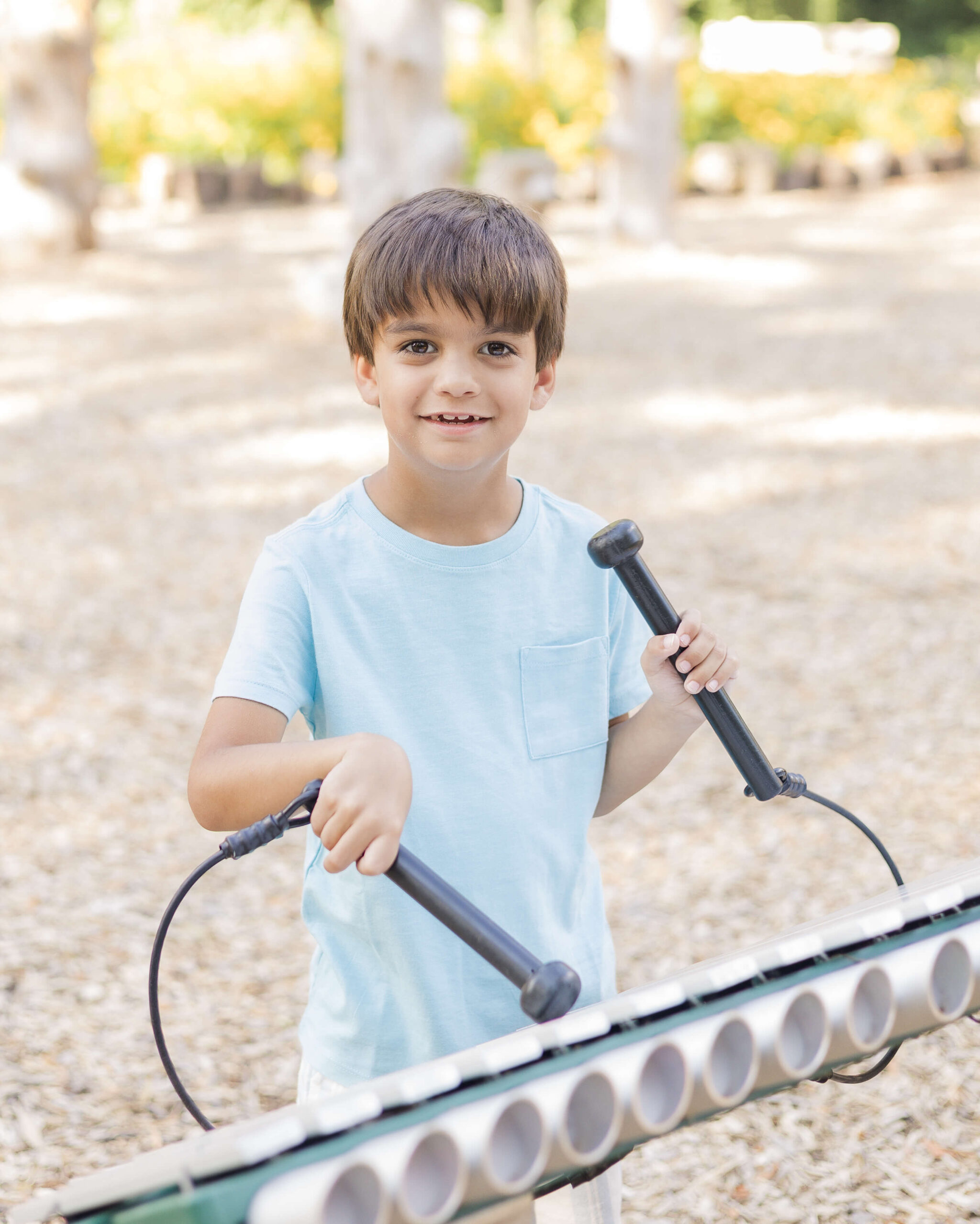 A toddler boy in a blue shirt plays a xylophone with a smile at one of the playgrounds in Springfield, IL