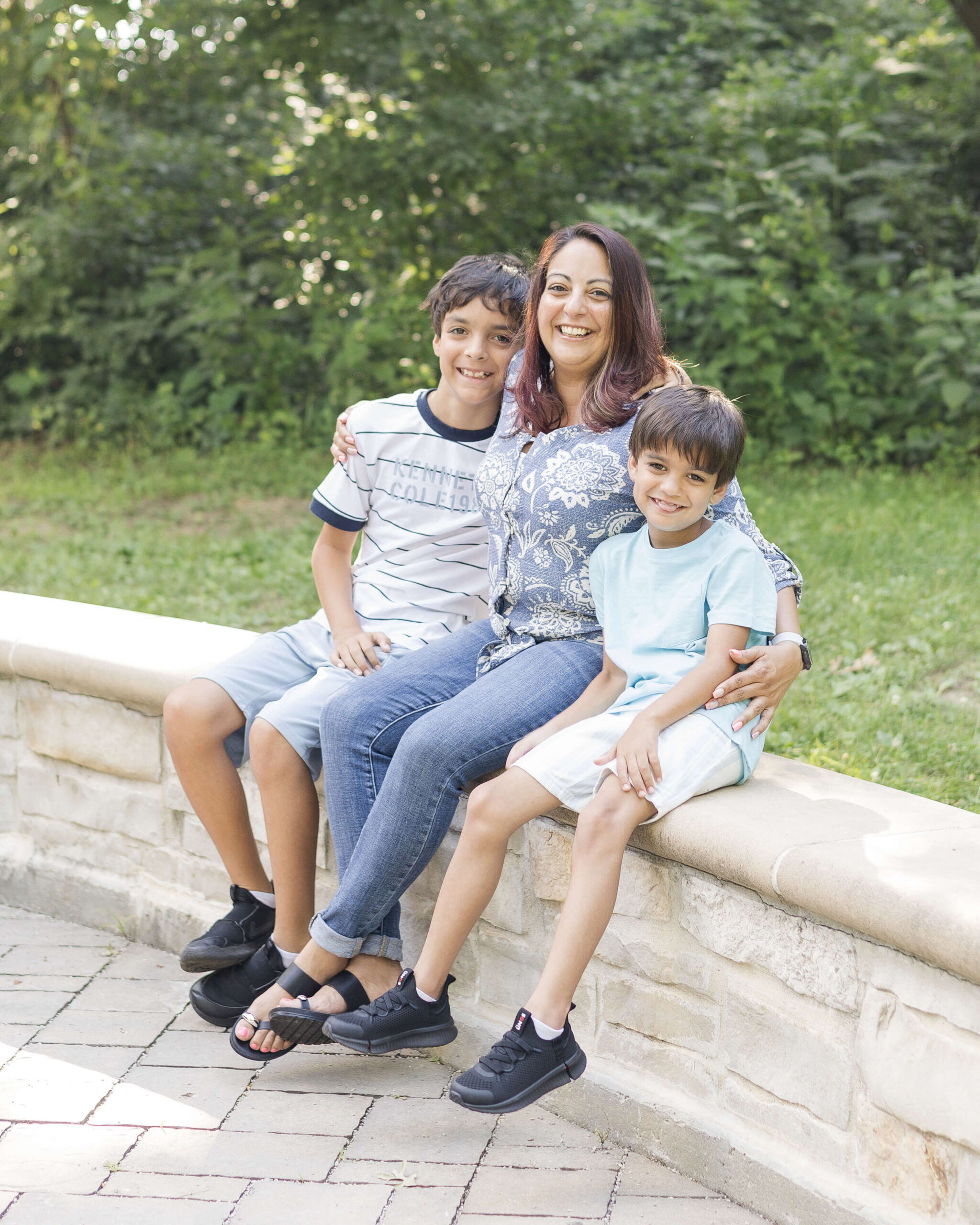 A smiling mother sits on a garden wall hugging her two young sons after visiting lincoln historic sites in springfield illinois