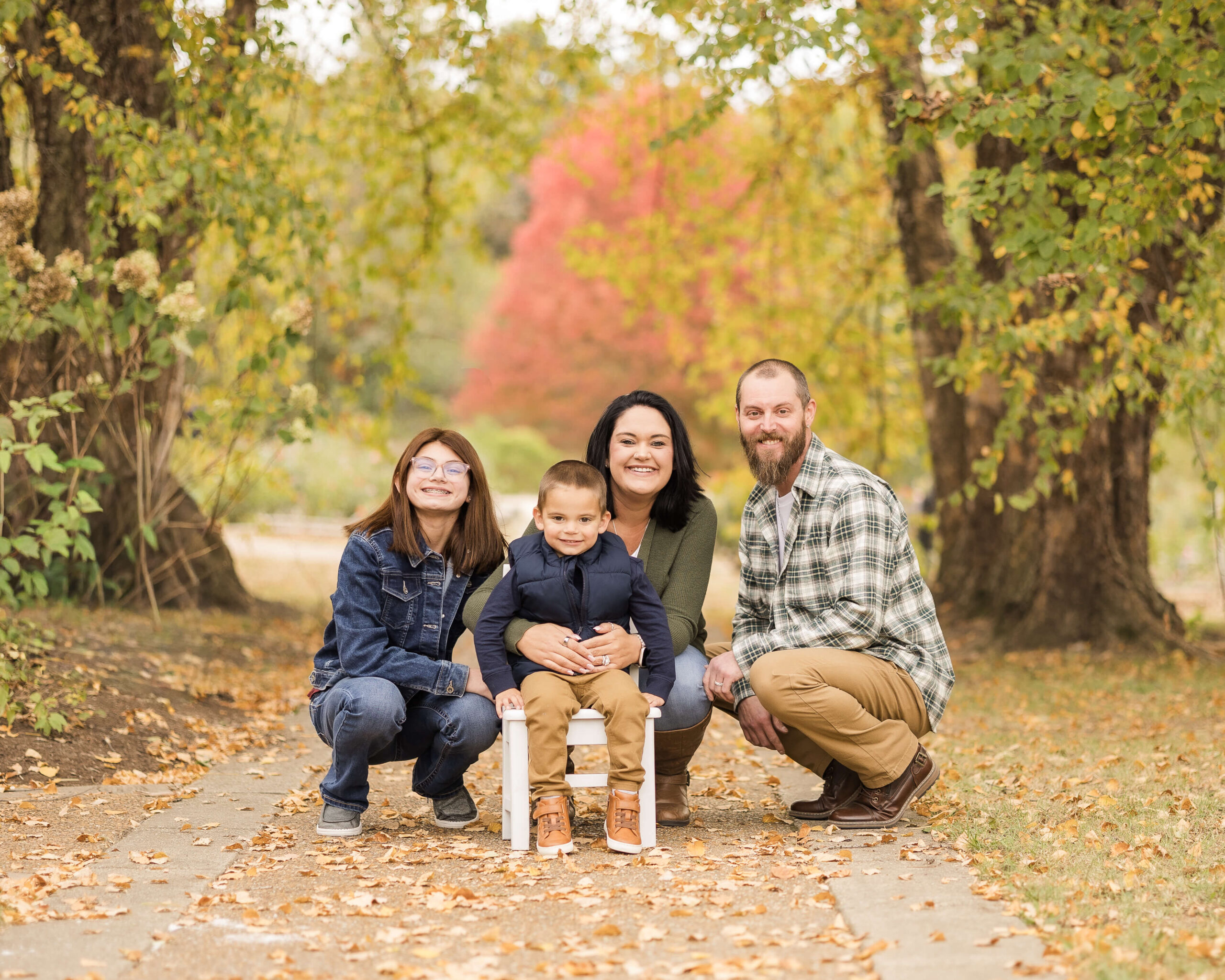 Happy mom and dad squat in a park path with their teen daughter and toddler son in fall after visiting preschools in springfield, il