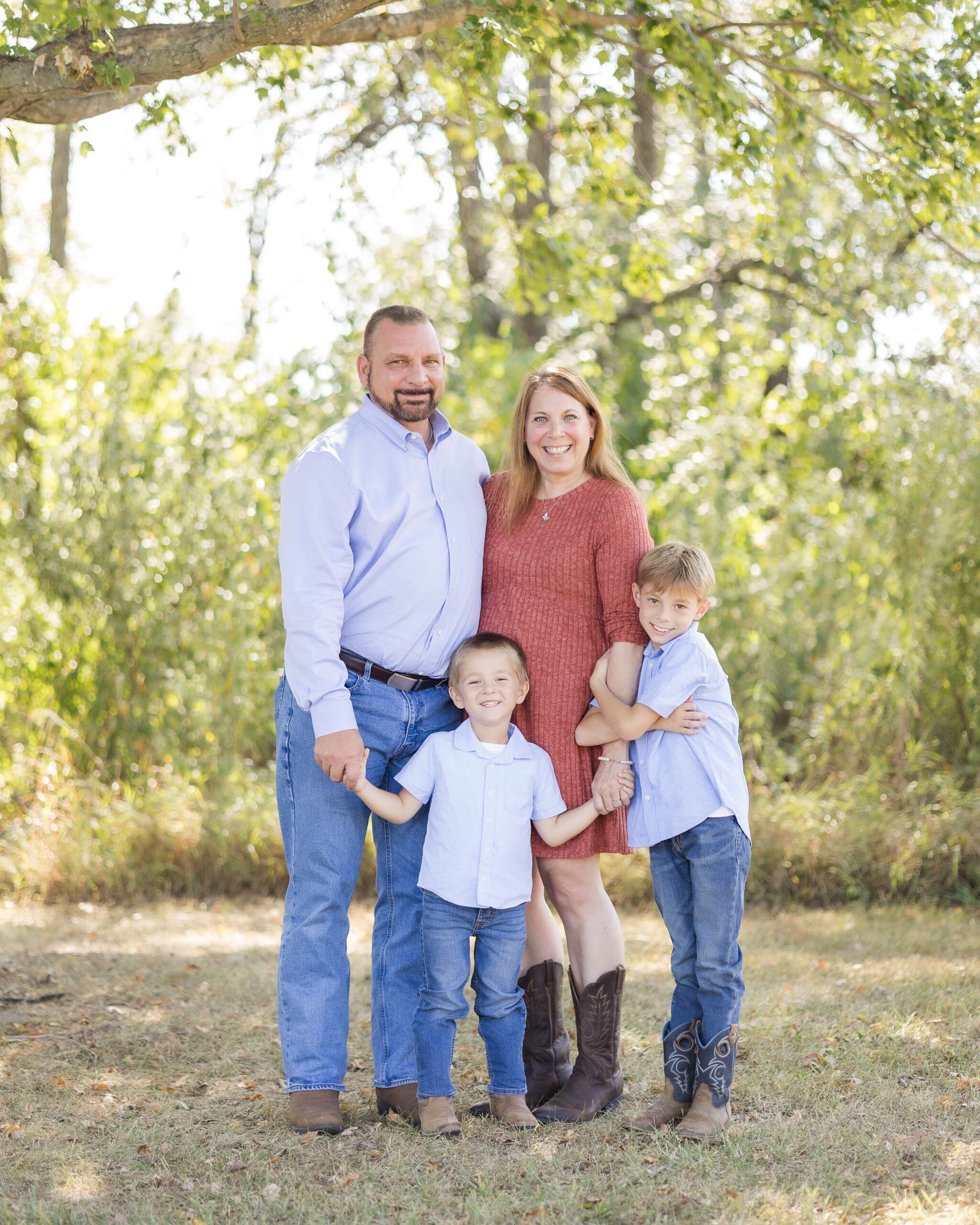 A grandma and grandpa smile while standing with their toddler grandsons in matching blue shirts and jeans