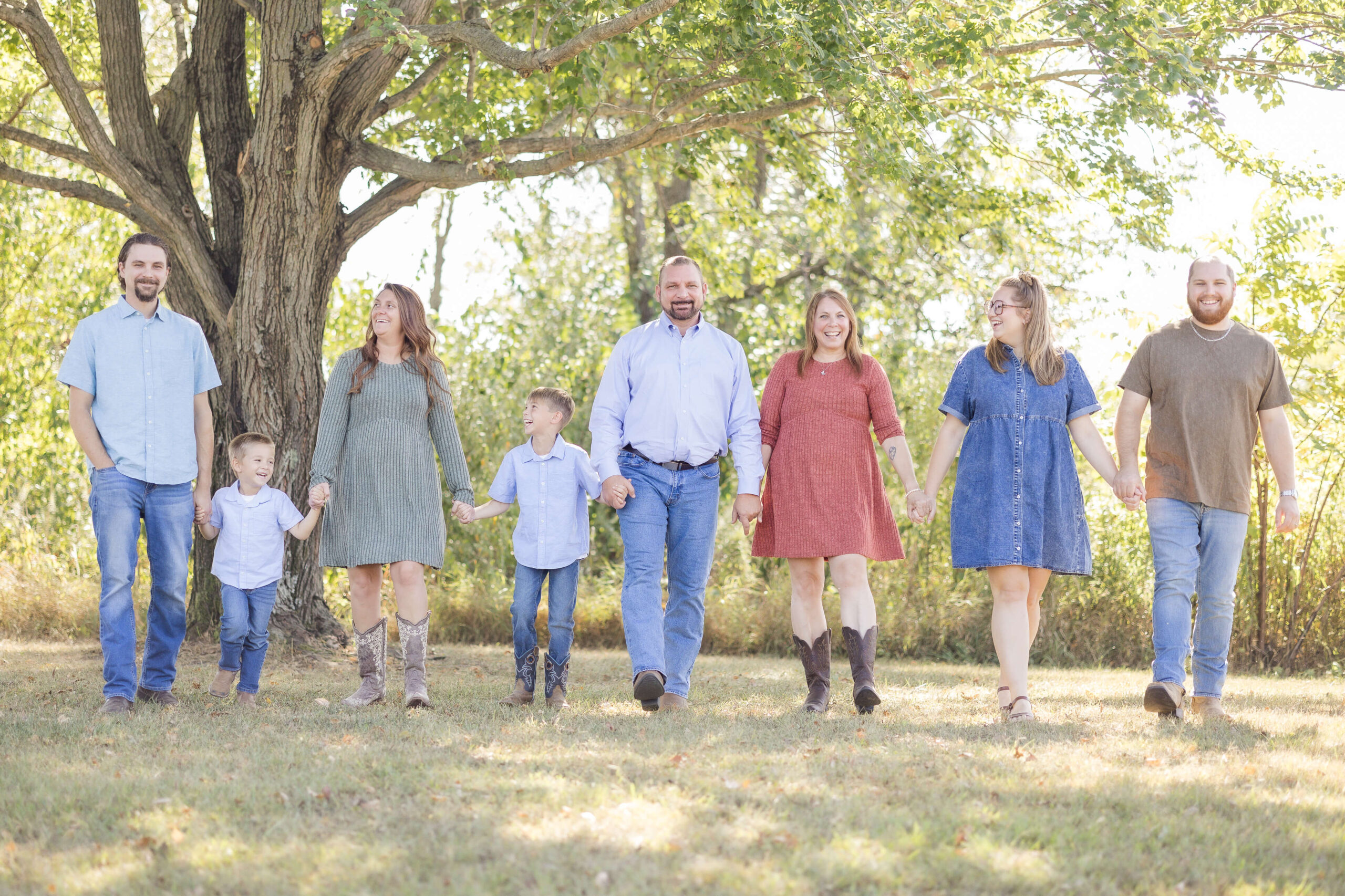 A large extended family walks while holding hands under a tree in a park while smiling and laughing with each other before heading to county fairs in illinois