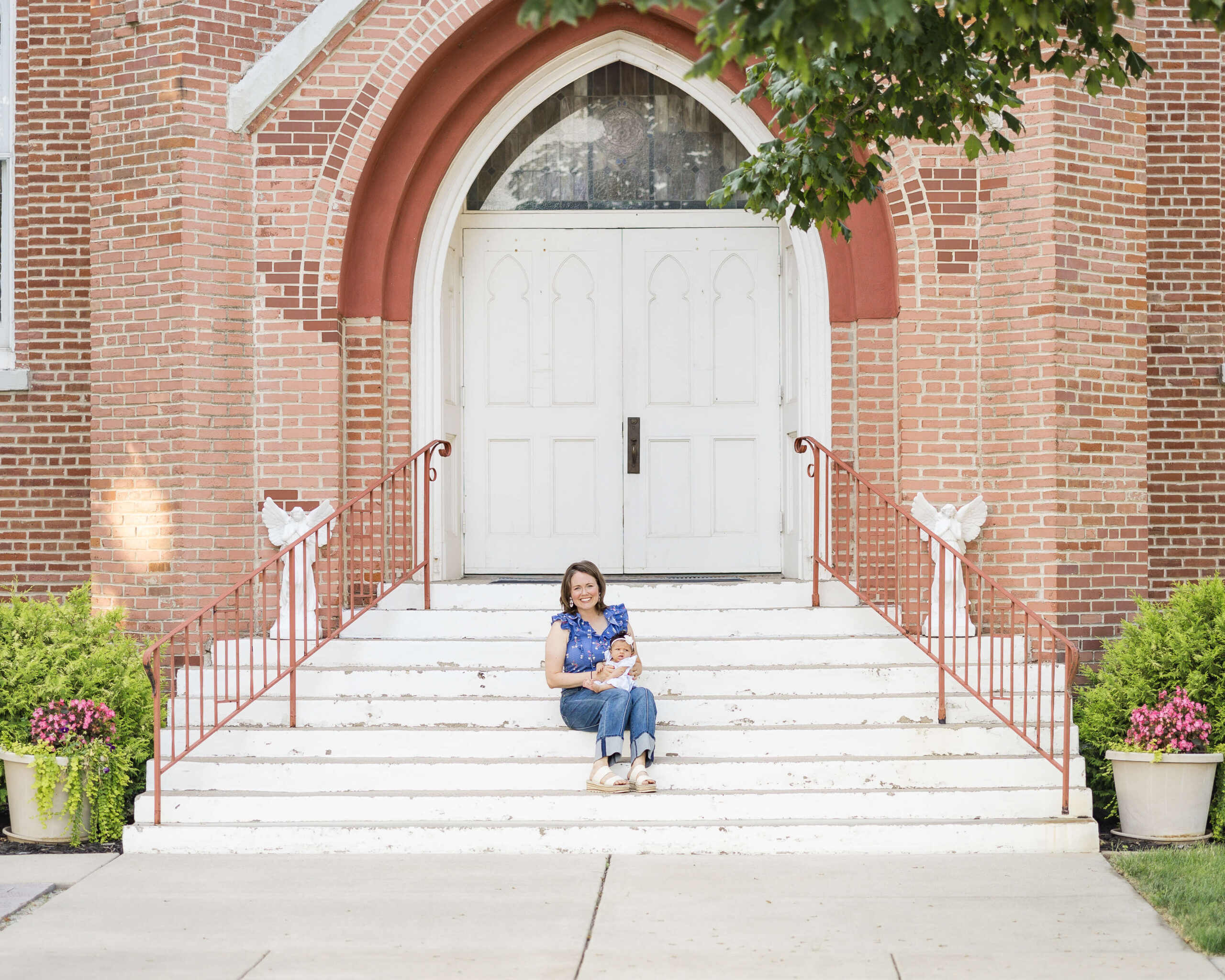 A happy mom sits on church steps with a newborn girl in her lap