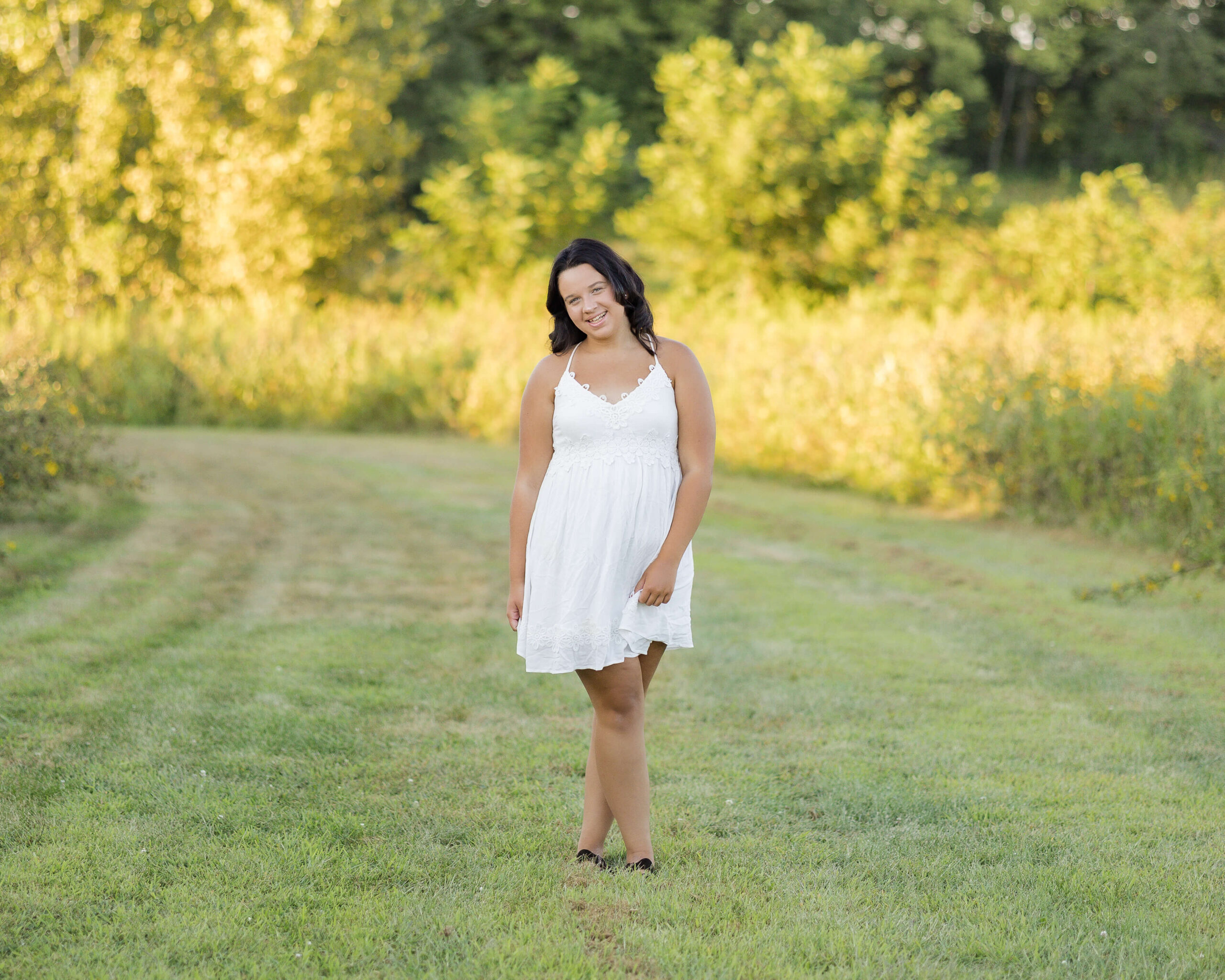 A woman with dark hair walks in a park trail at sunset while smiling