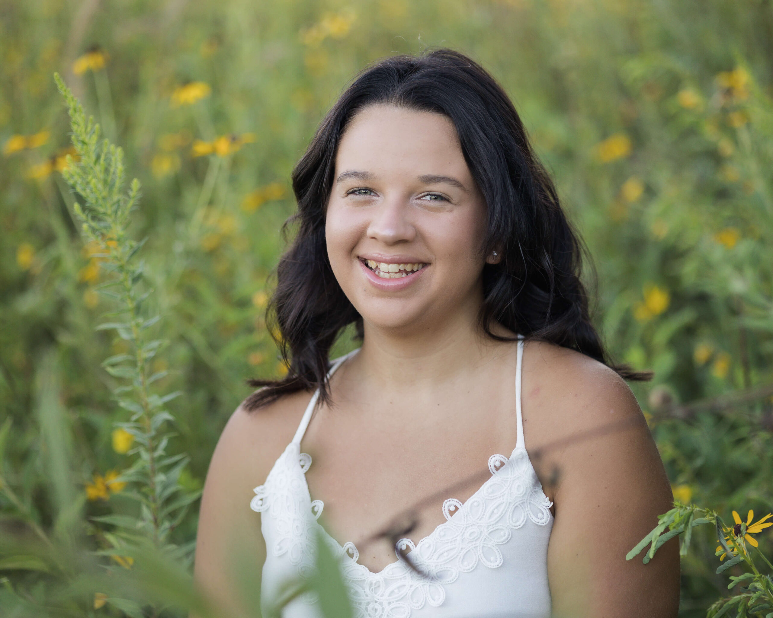 A woman smiles in a white dress while sitting in a field of yellow wildflowers after discovering high school volunteer opportunities in springfield il