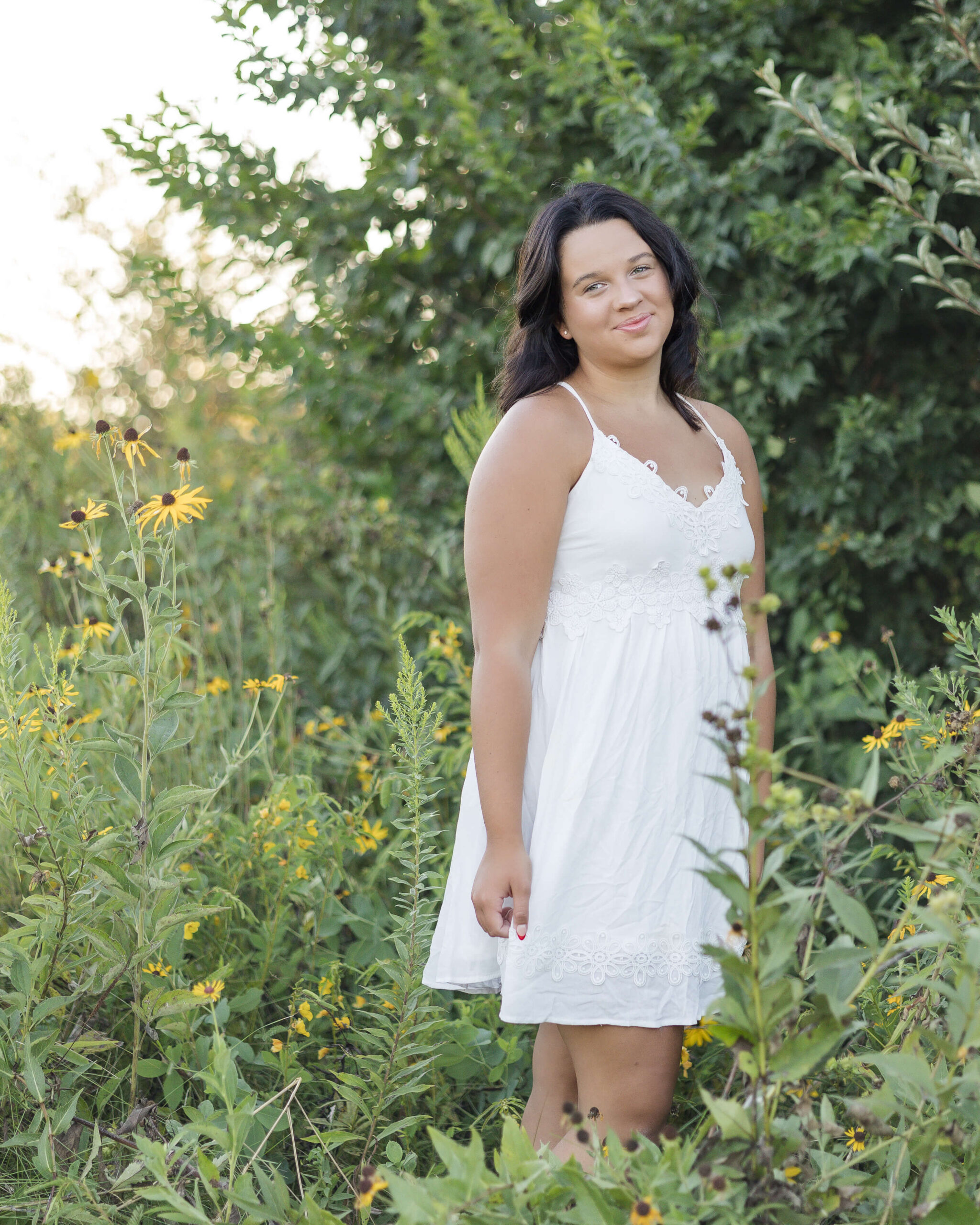 A woman in white stands among some yellow wildflowers smiling after exploring great high school volunteer opportunities in springfield il