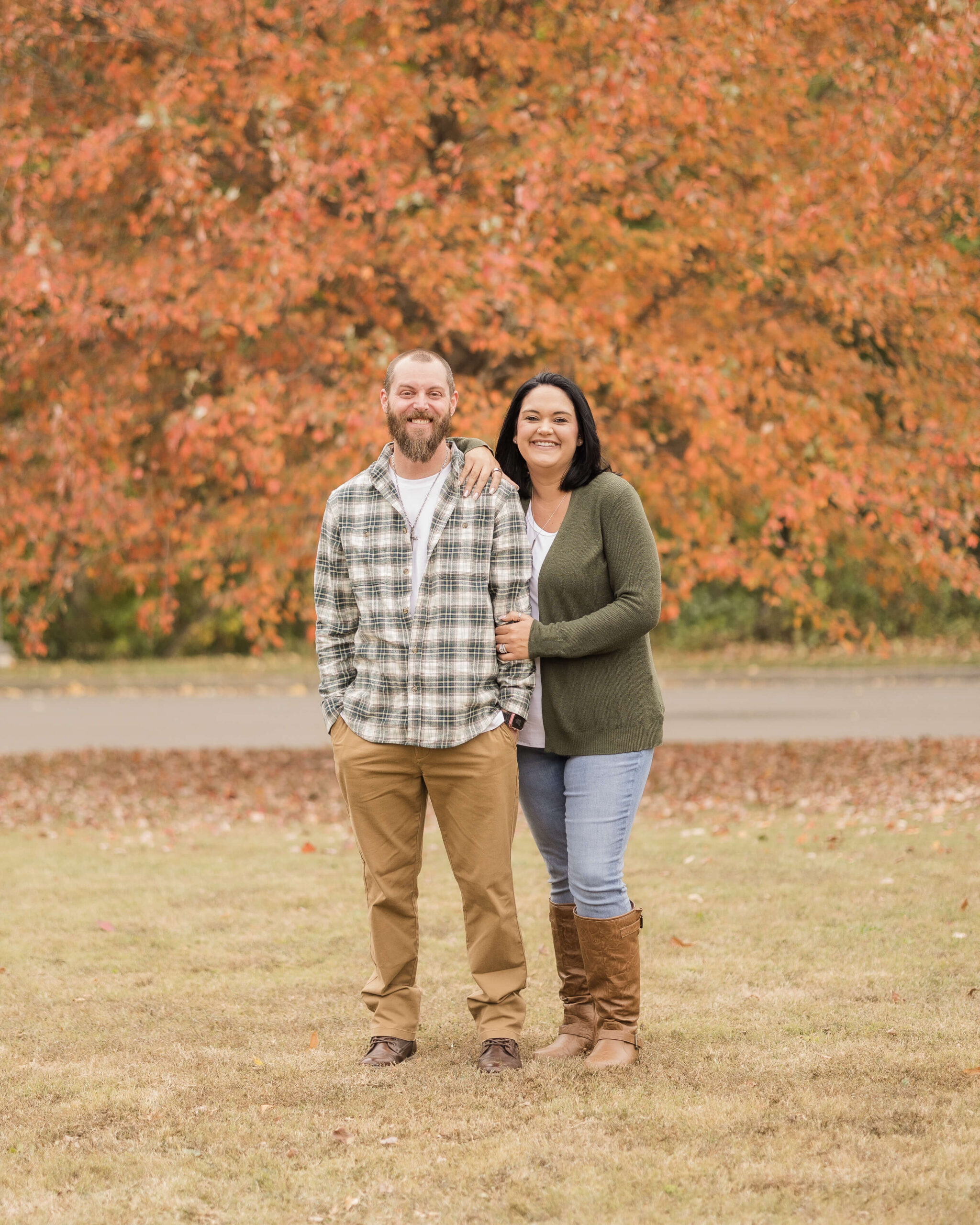 A happy couple smile in a park in fall in a plaid shirt and green sweater