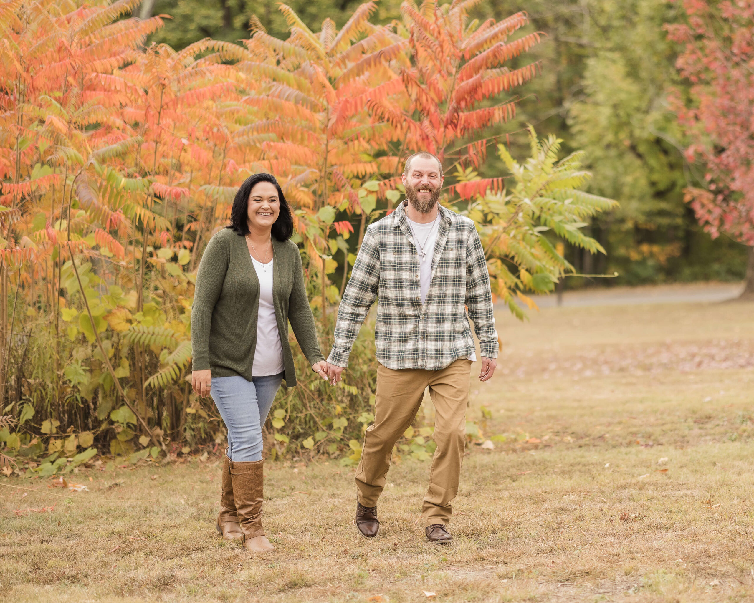 A happy couple hold hands and walk in a park in fall in plaid and green sweater after exploring music venues in springfield il