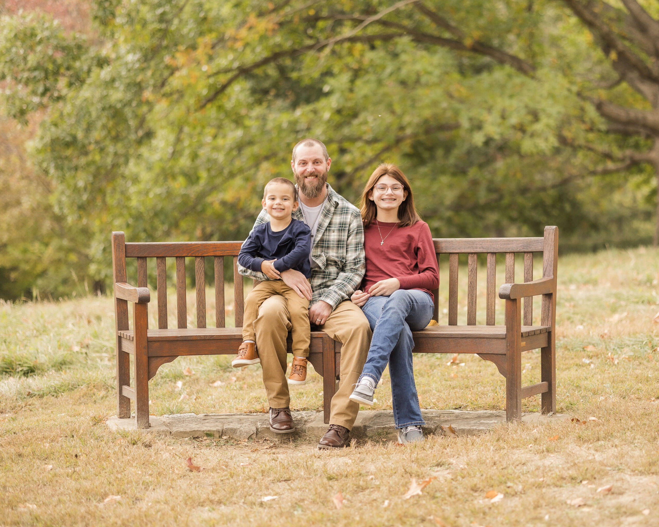 Happy dad in plaid sits on a park bench with his teen daughter and toddler son