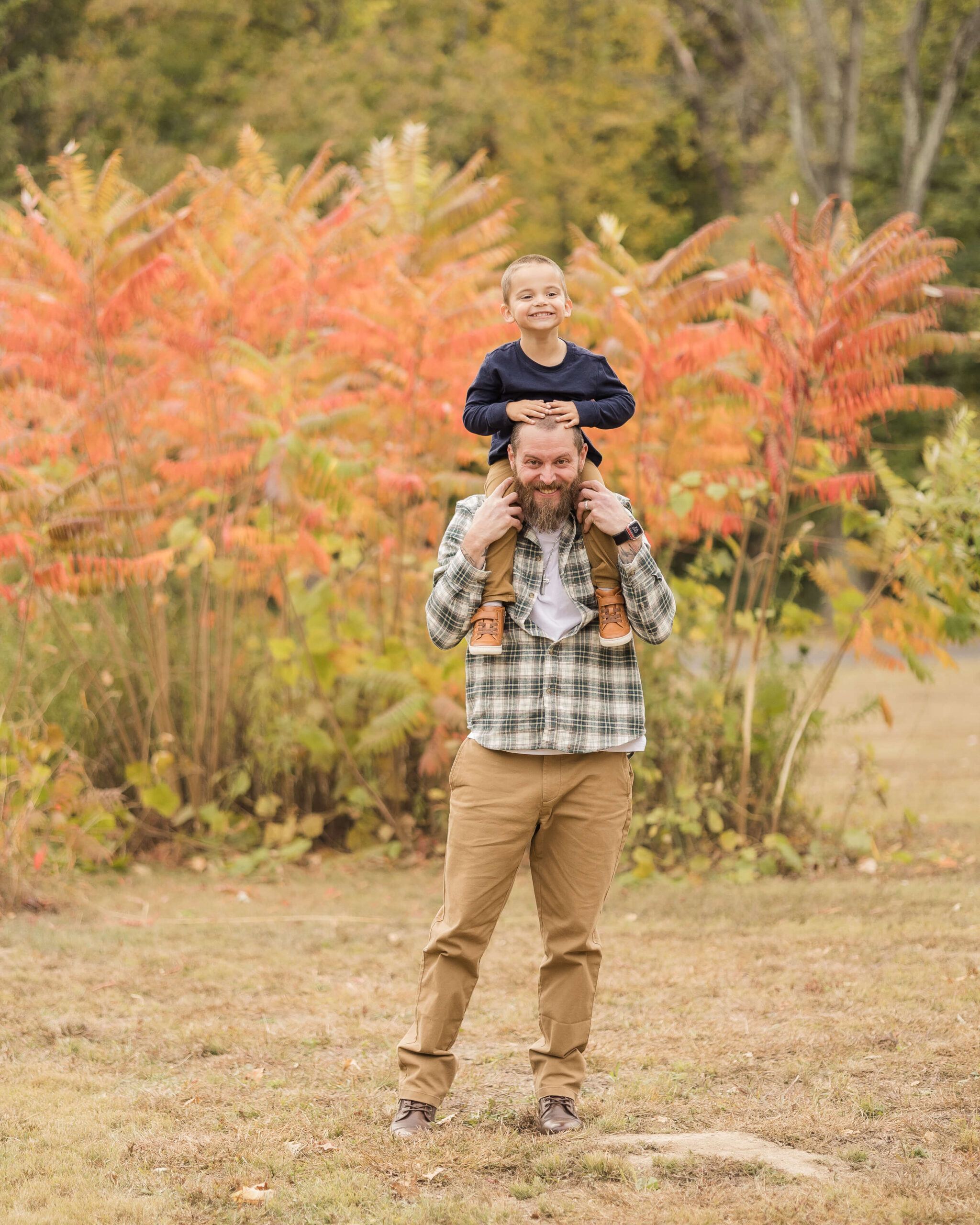A smiling father in green plaid stands in a park with his toddler son giggling on his shoulders after exploring route 66 attractions in springfield il