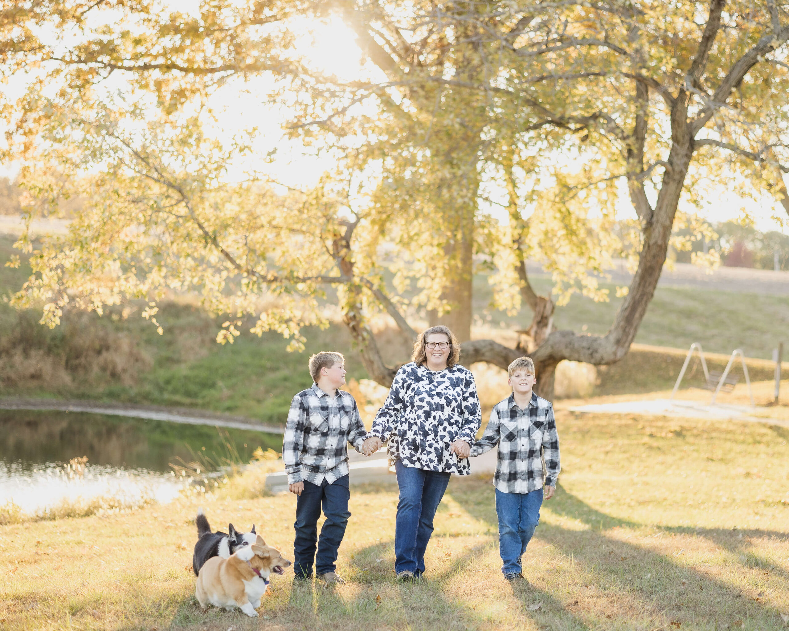A smiling mother walks in a park by a pond holding hands with her two young sons in matching black and white plaid at sunset before exploring things to do at the illinois state fair