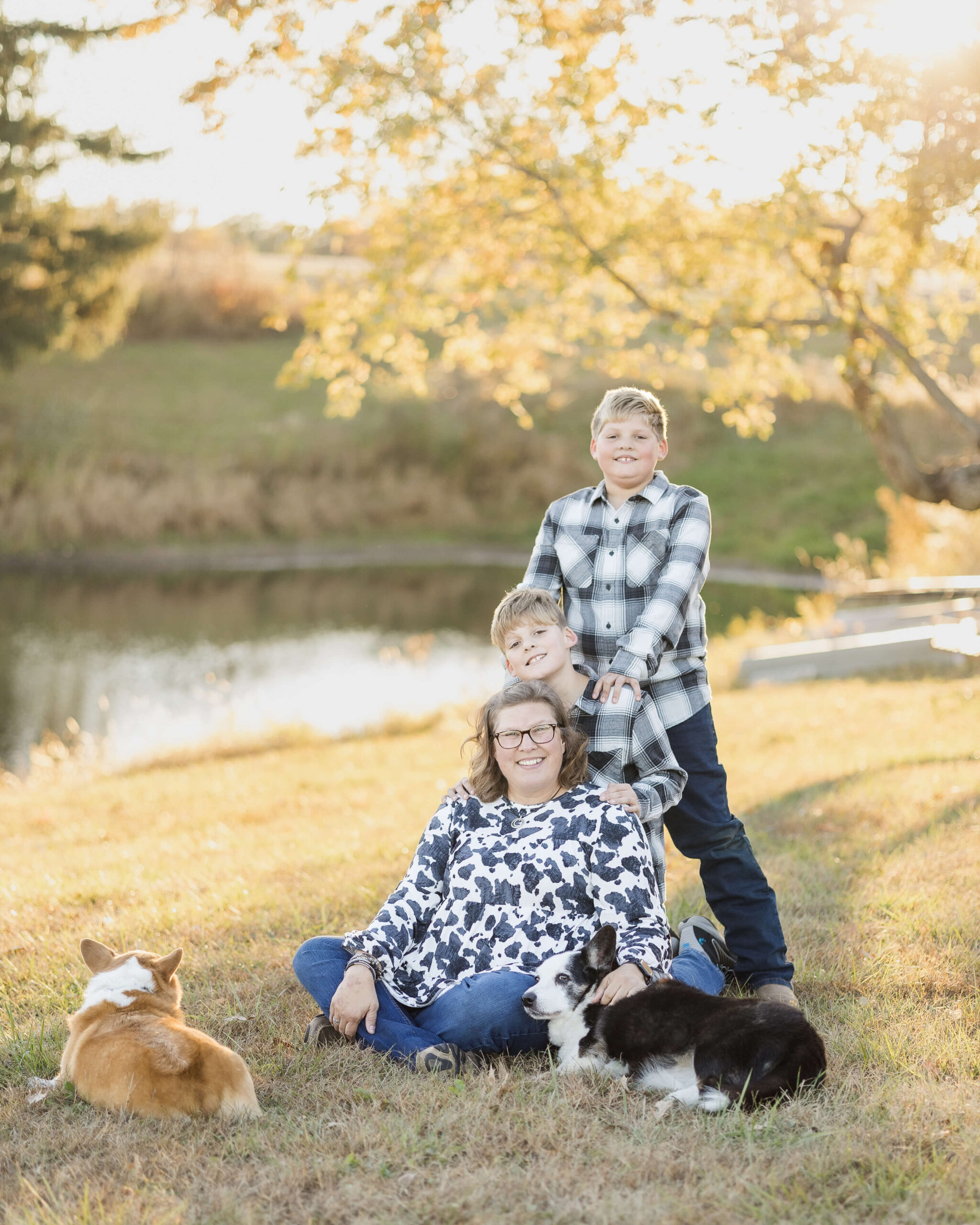 A happy mom sits in the grass with two corgies with her two young sons standing behind her by a pond before enjoying things to do at the illinois state fair