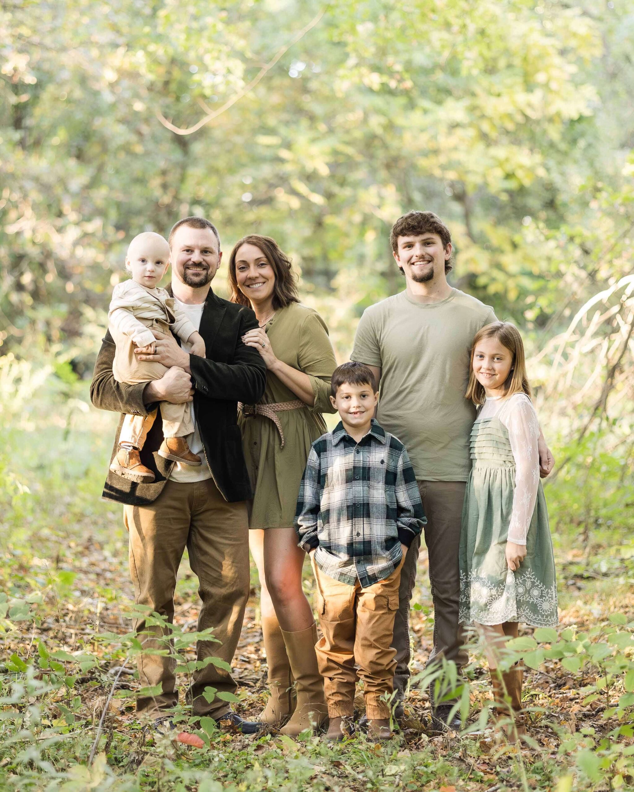 Happy mom and dad stand in a park with their four children smiling and hugging