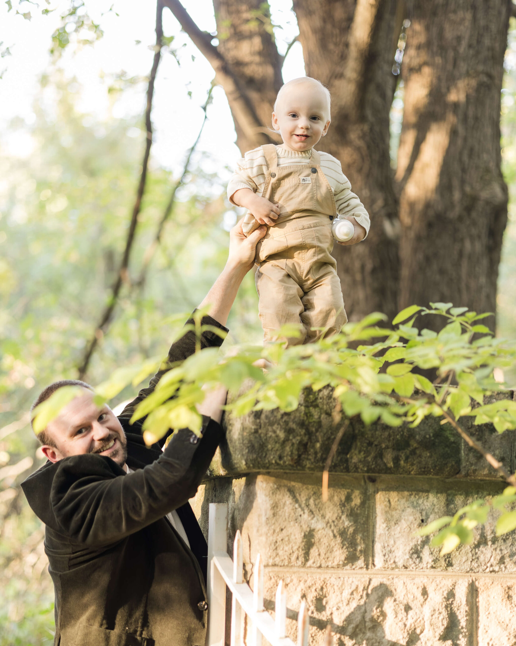 A happy dad reaches for his toddler son walking on a wall in a park after visiting children's museums in Springfield, IL