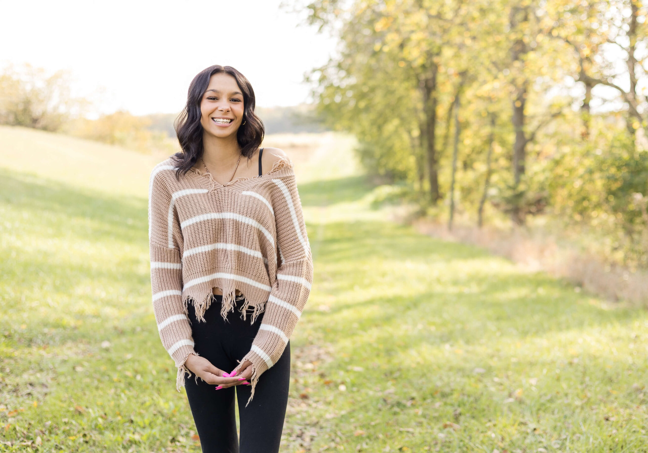 A happy high school senior laughs while walking in a meadow at sunset