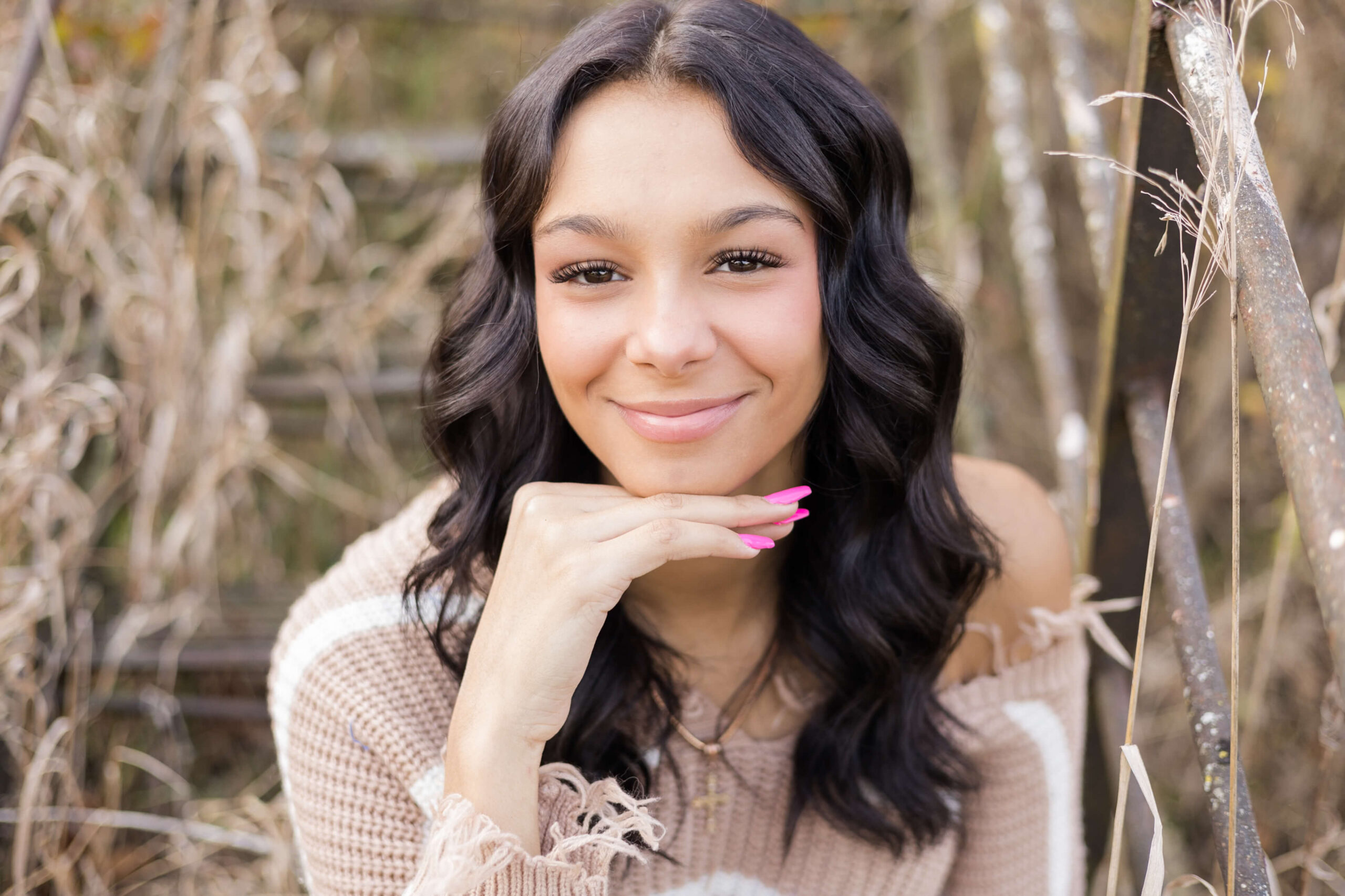 A closeup look at a smiling high school senior in a tan knit sweater in tall grass after loving summer camps in Springfield, IL