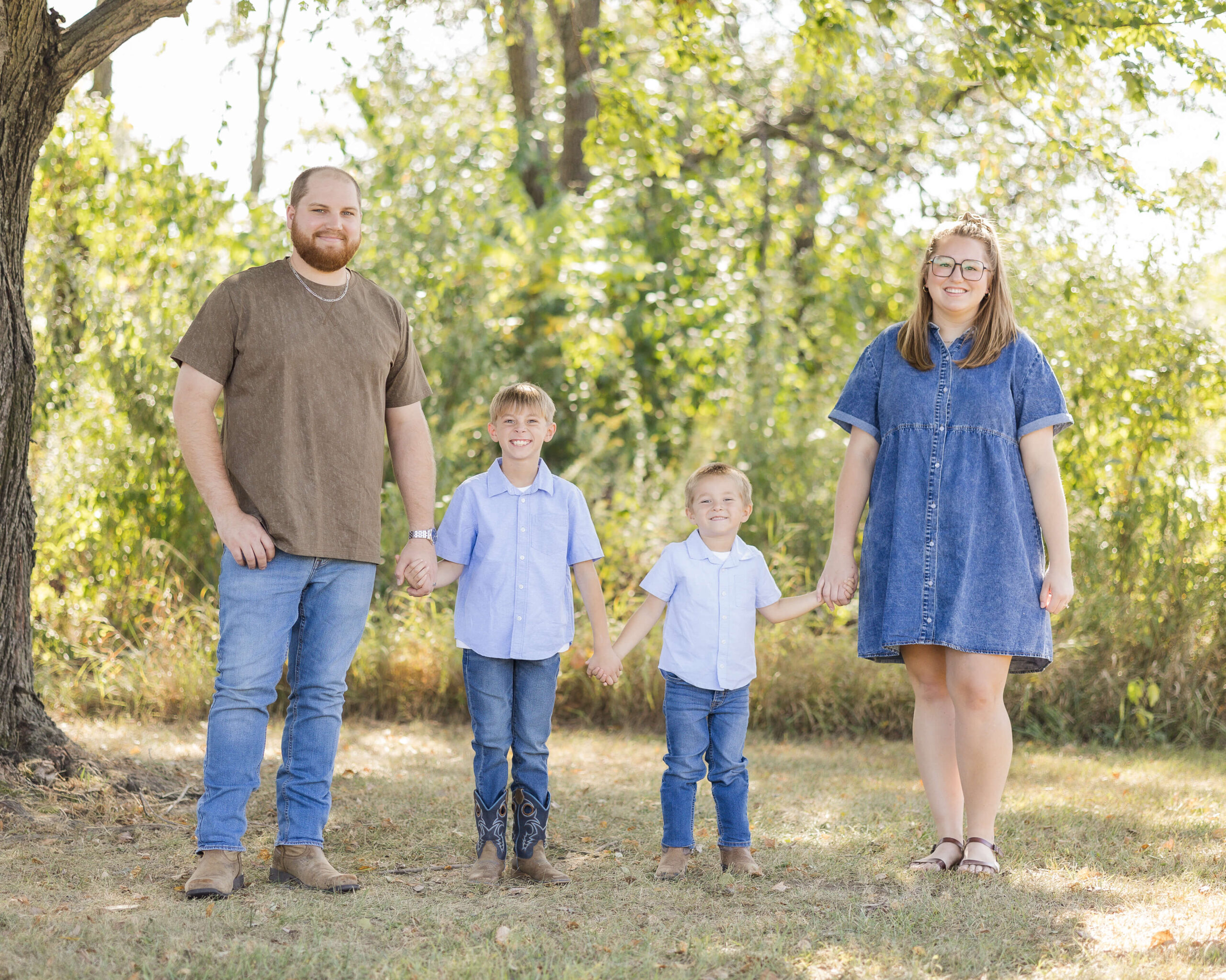 A mom and dad walk in a park holding hands in denim with their matching toddler sons before some summer camps in Springfield, IL
