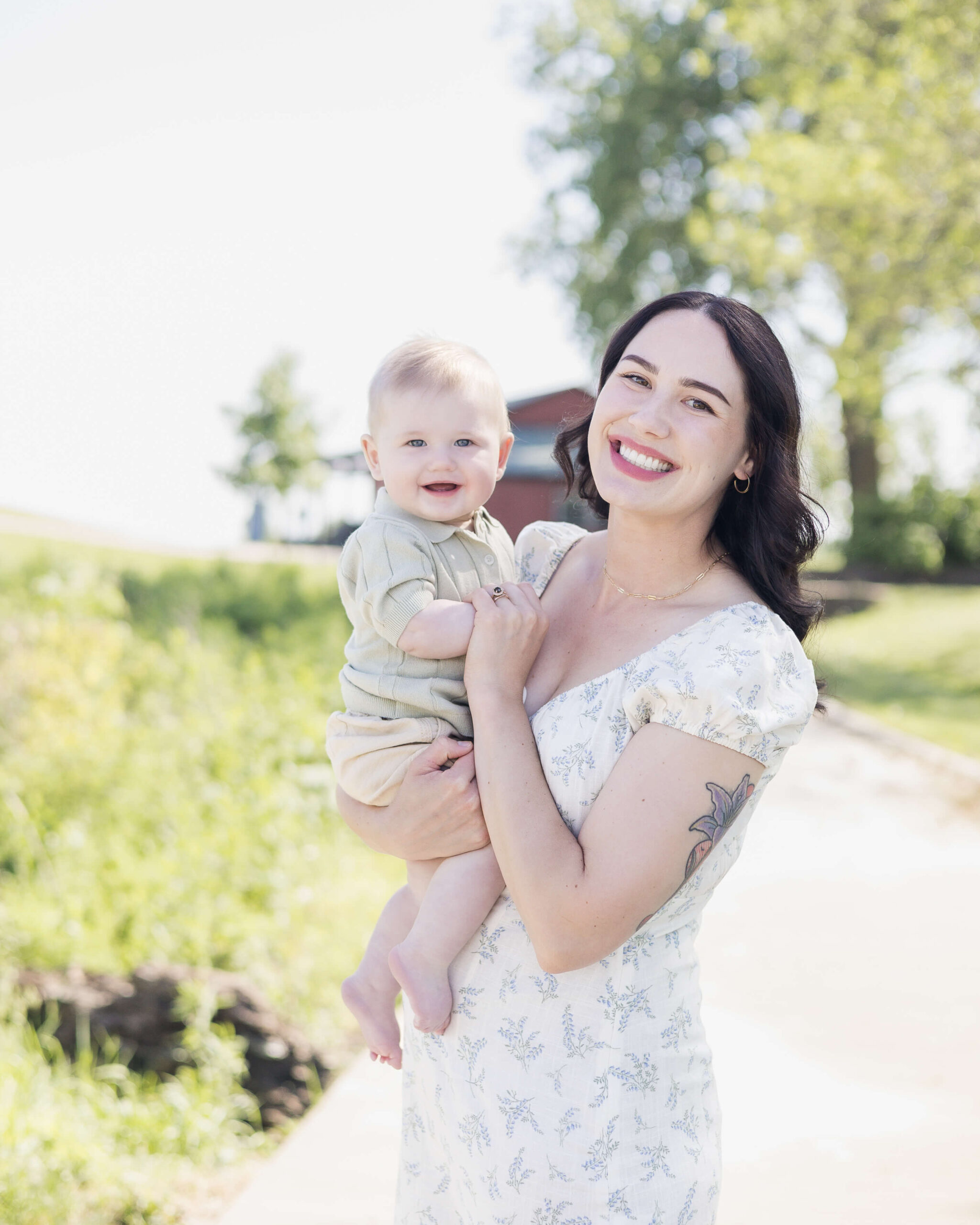 A happy mother in a white floral dress smiles while holding her infant smiling son in her arms after some swim lessons in Springfield, IL