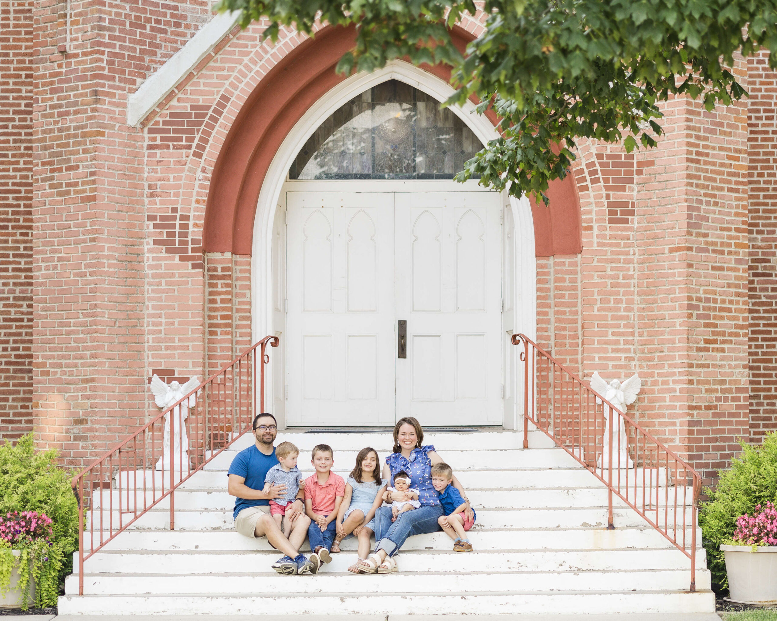 A happy mom and dad sit on church steps with their five toddlers