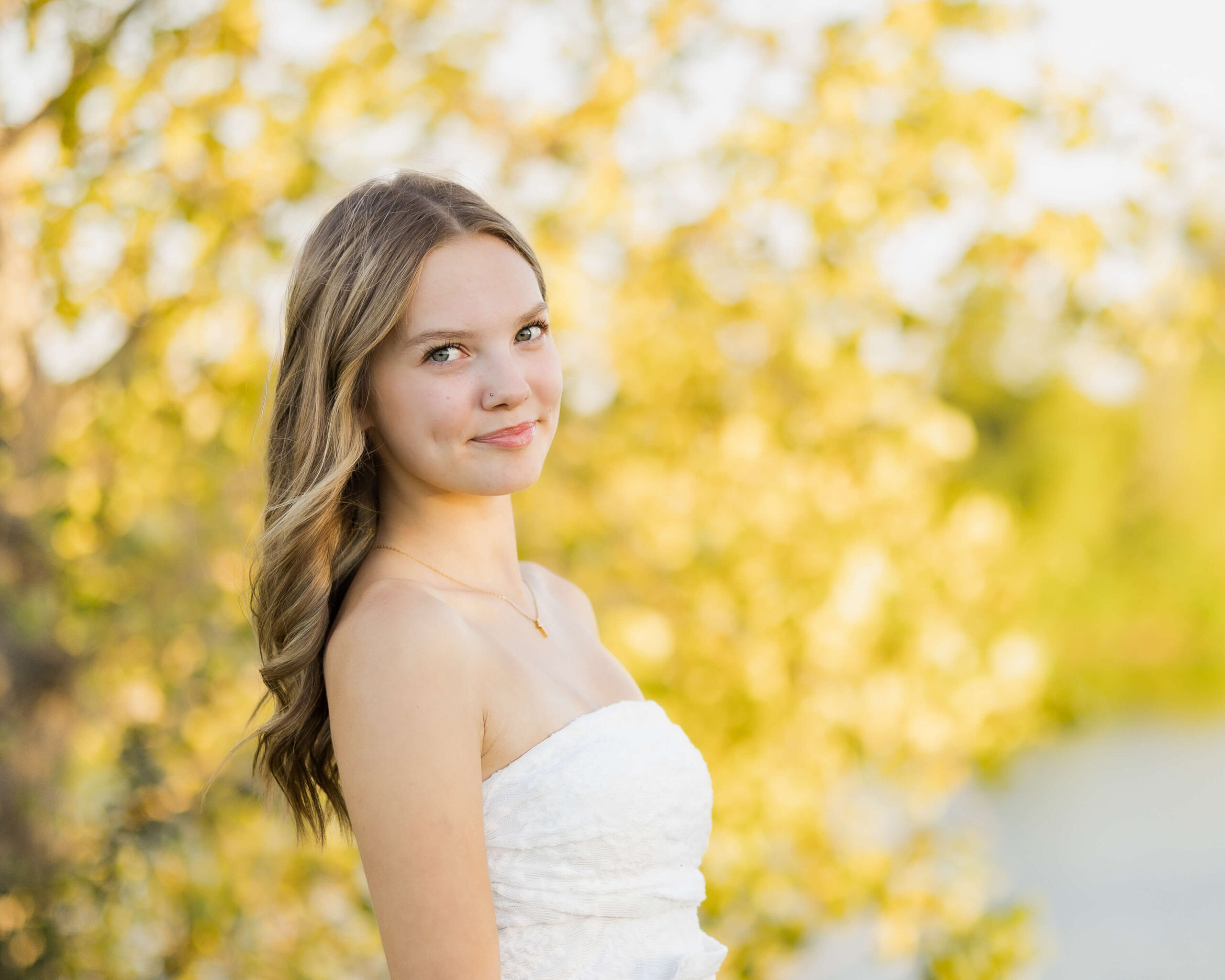 A high school senior in a white blouse stands at sunset by a pond after visiting graduation party venues in springfield il
