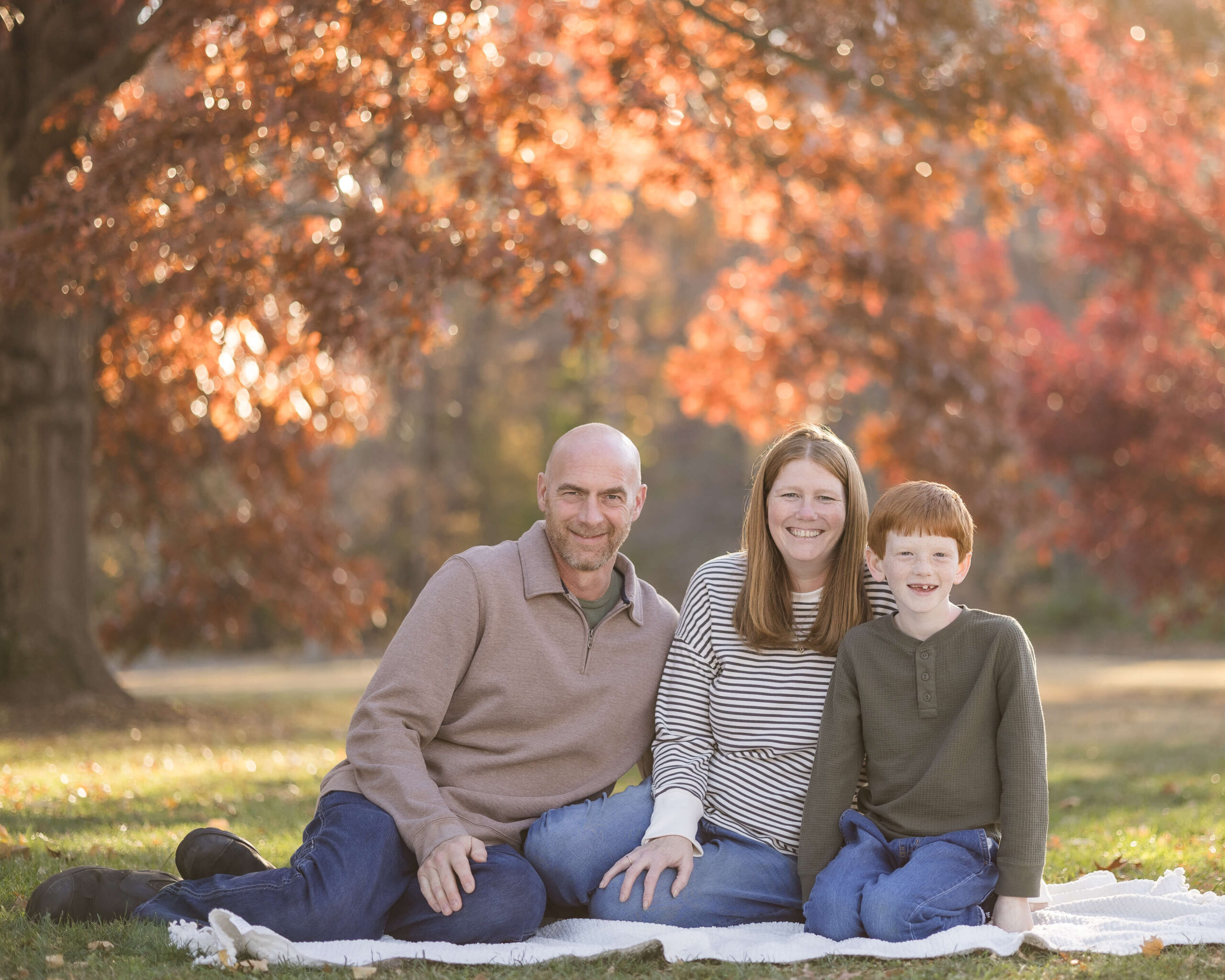 Happy mom and dad sit on a picnic blanket in a park with their young son before visiting indoor playgrounds in springfield il