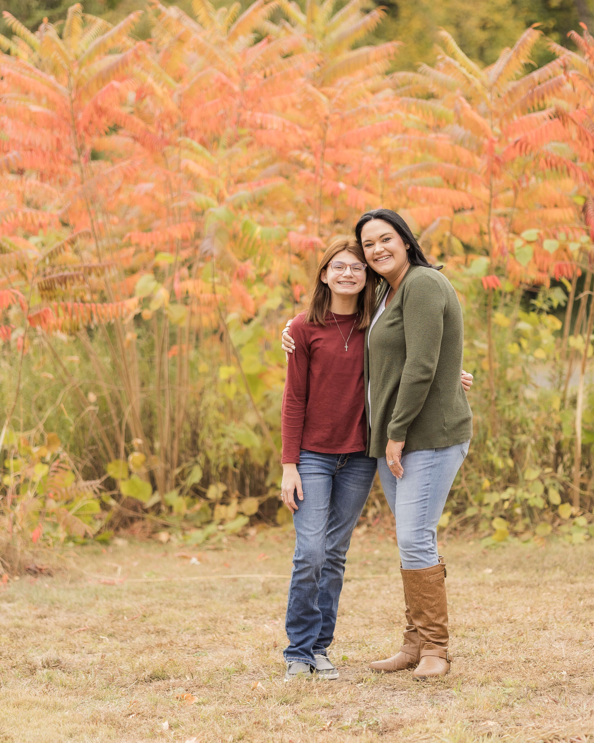A happy mom in green hugs her young teen daughter in a park in fall before heading to kid friendly restaurants in springfield il