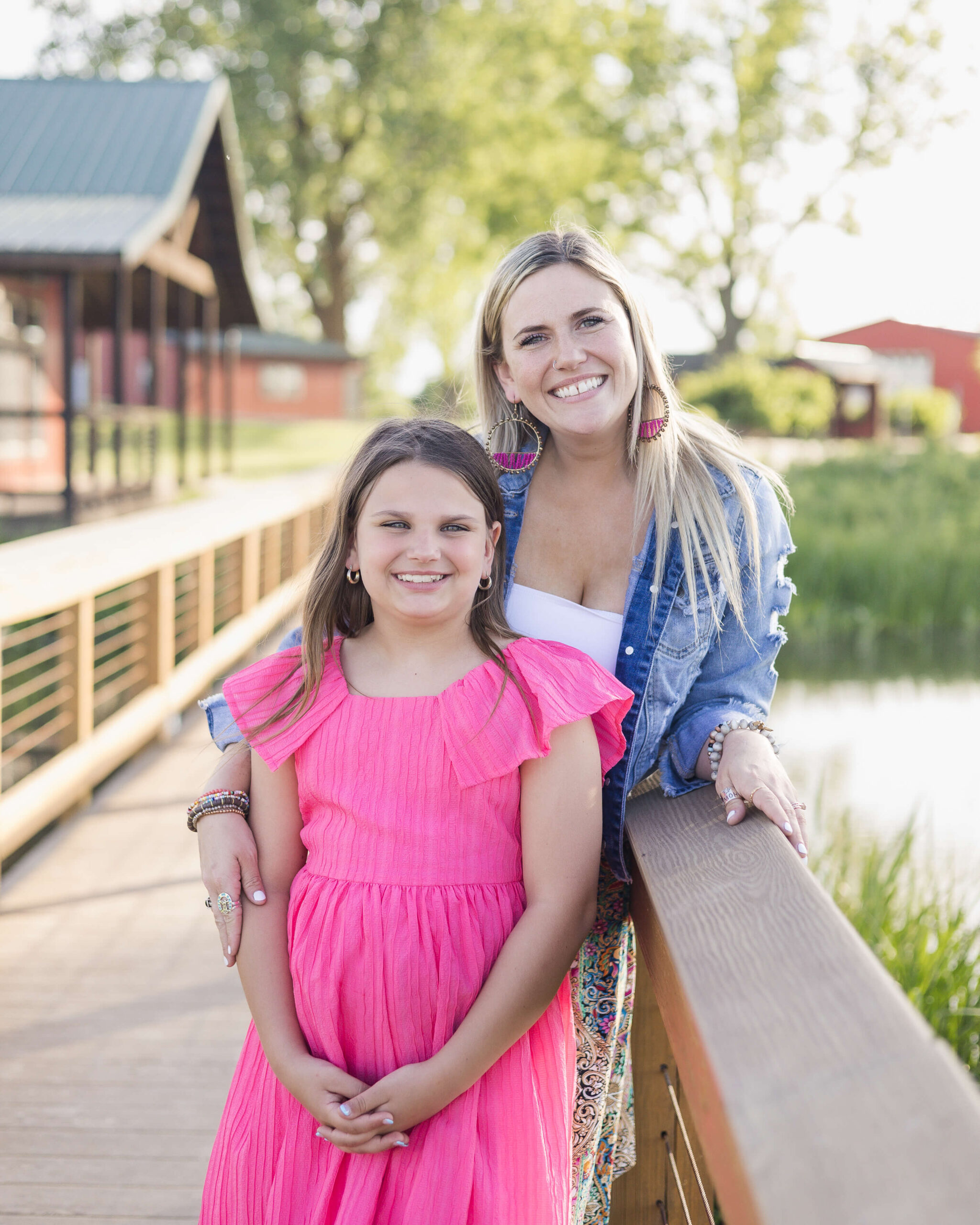 A happy mom stands on a boardwalk over a pond with her young daughter in a pink dress after some spring break camps springfield, IL