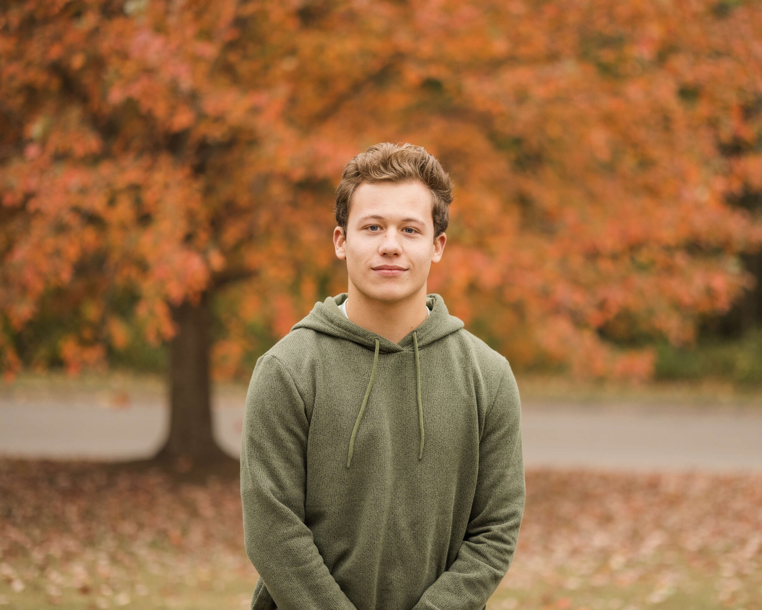 A high school senior in a green hoodie stands smiling in a park in fall after finding great test prep in springfield il