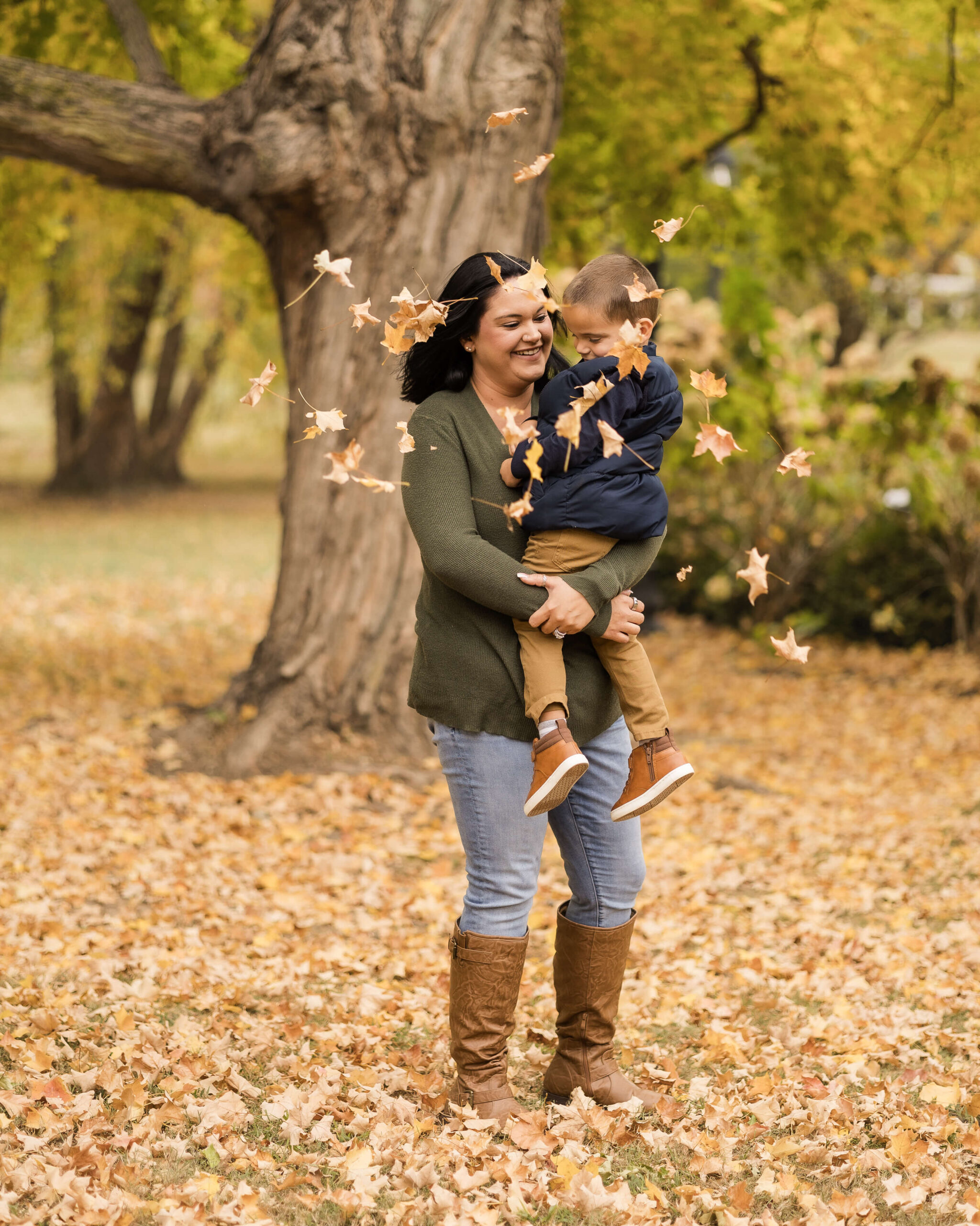 A mother plays in the fallen leaves with her toddler son in a park before visiting a trampoline park in springfield il