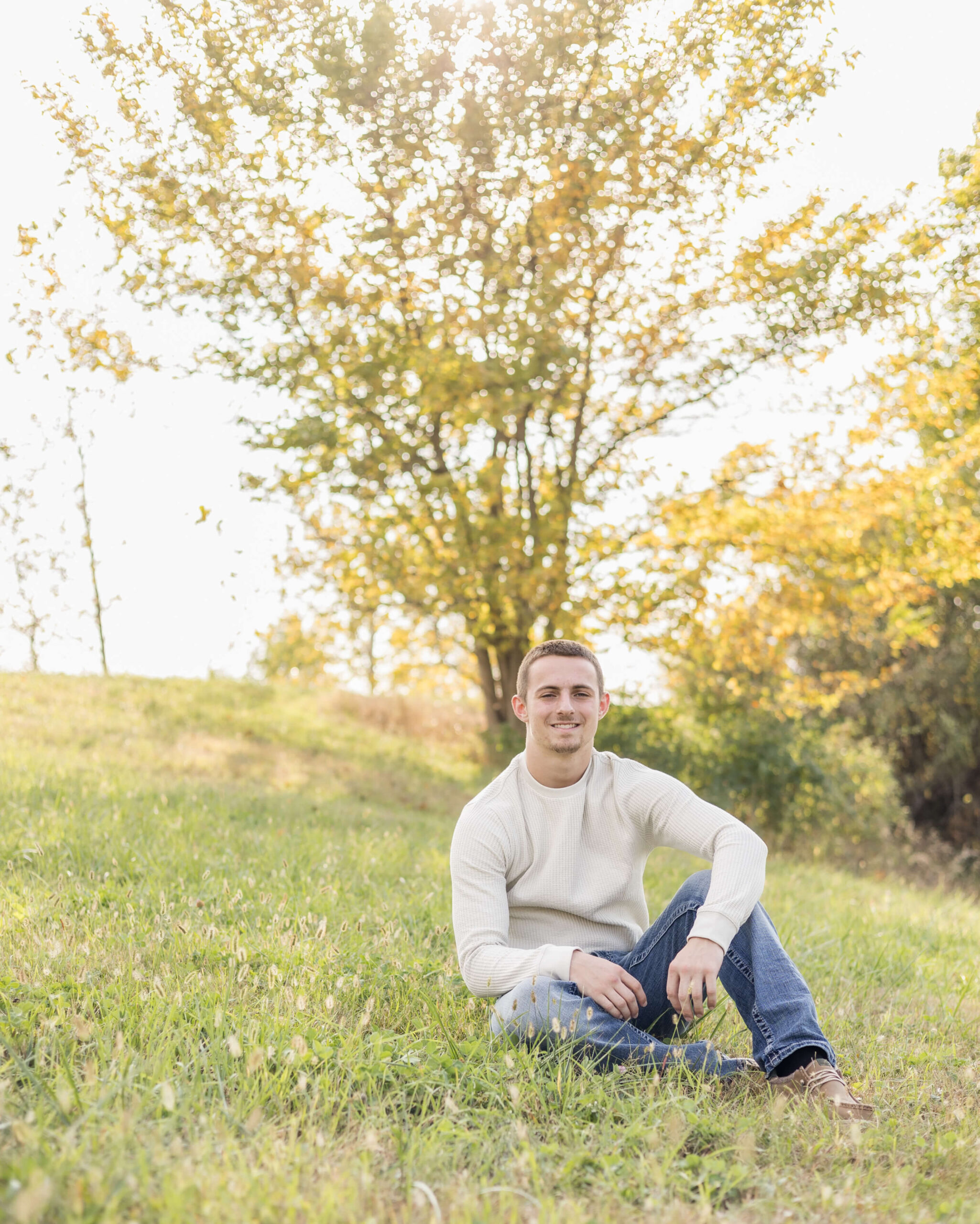 A high school senior sits smiling on a hillside at sunset in a cream shirt after finding great tutoring in springfield il