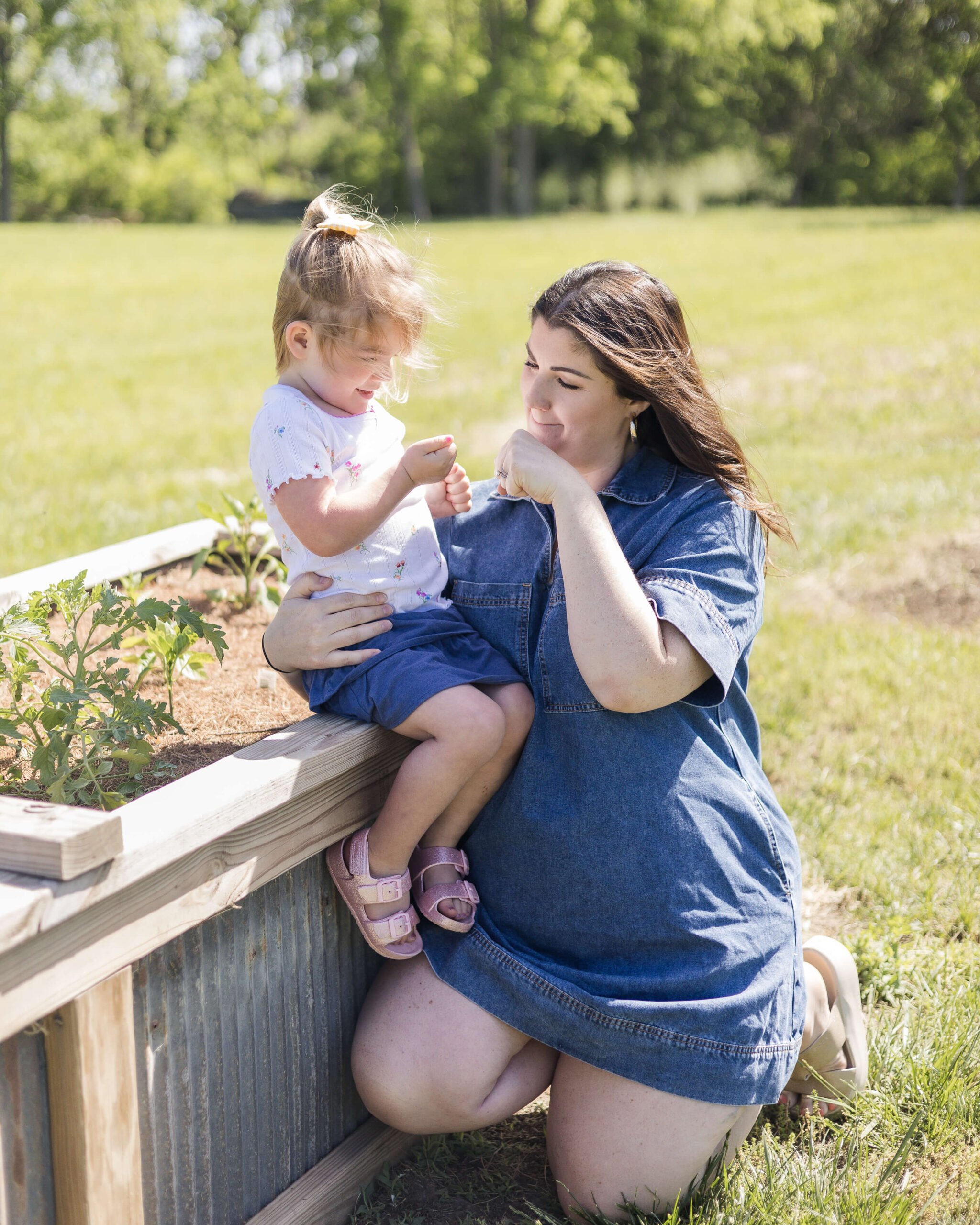 A mom fist bumps her toddler daughter sitting on a raised garden ben in denim after exploring birthday party places in Springfield, IL
