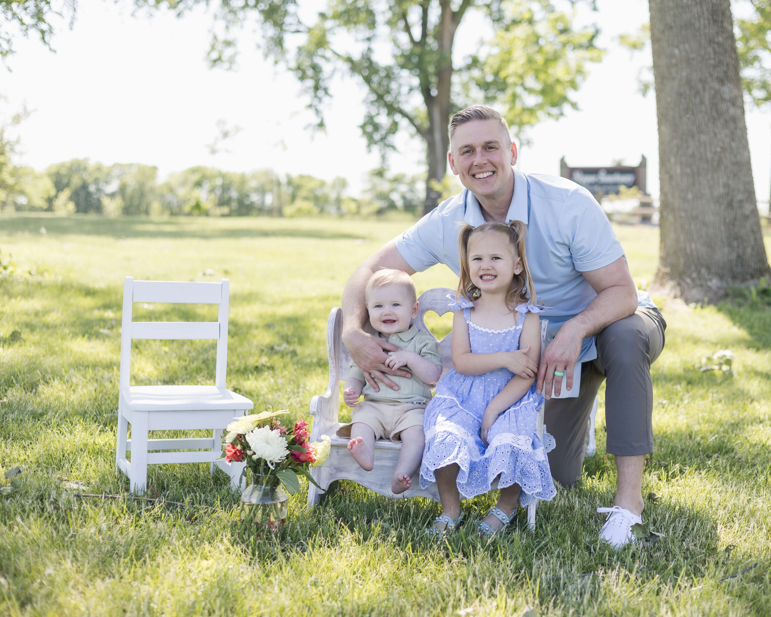 A happy dad hugs his toddler daughter and son on a tiny bench in a park after easter brunch in springfield il