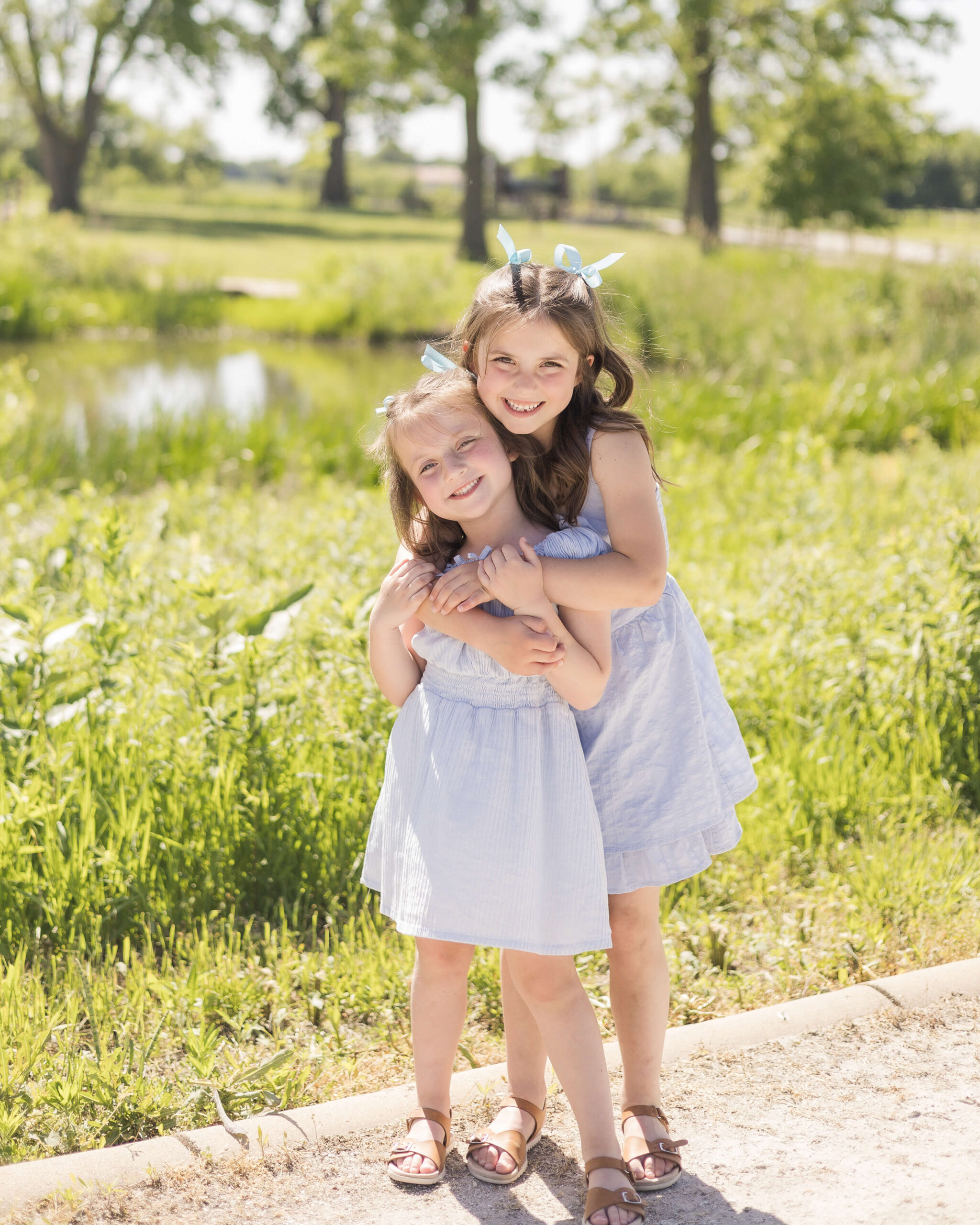 Toddler sisters in matching blue dresses hug in a park path with big smiles after enjoying easter egg hunts in springfield il
