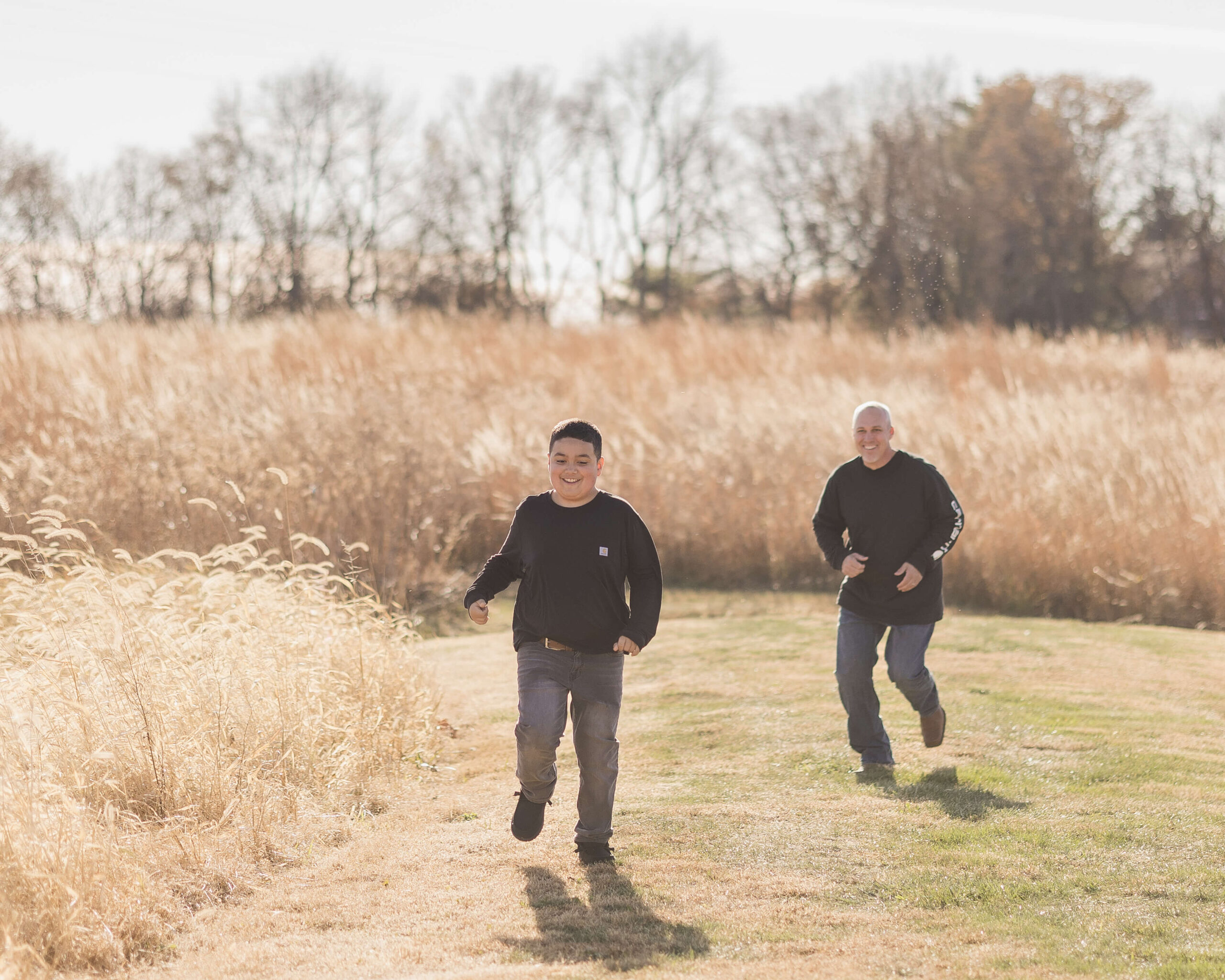 A young boy runs from dad in a park trail through fields of grain