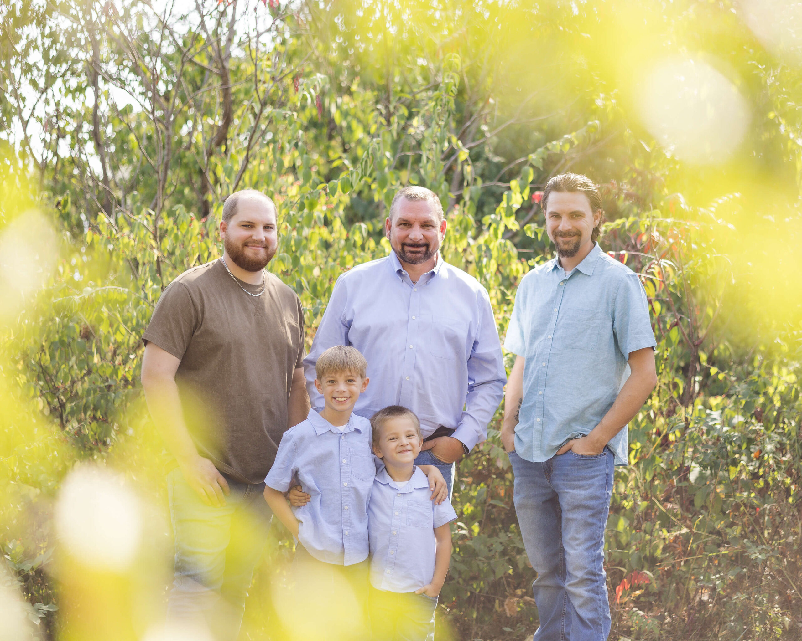 A dad stands with his four sons adult and toddler in a garden at sunset after some strawberry picking in central illinois